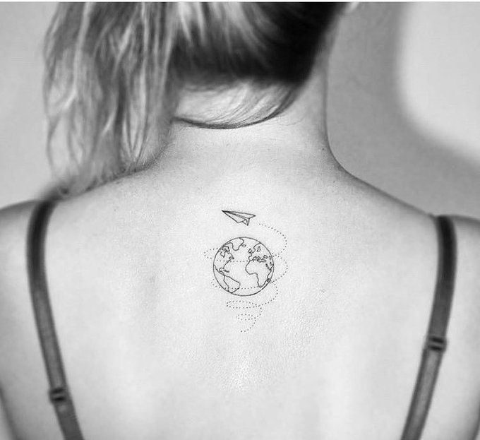 the back of a woman's neck with a small earth tattoo on her left shoulder