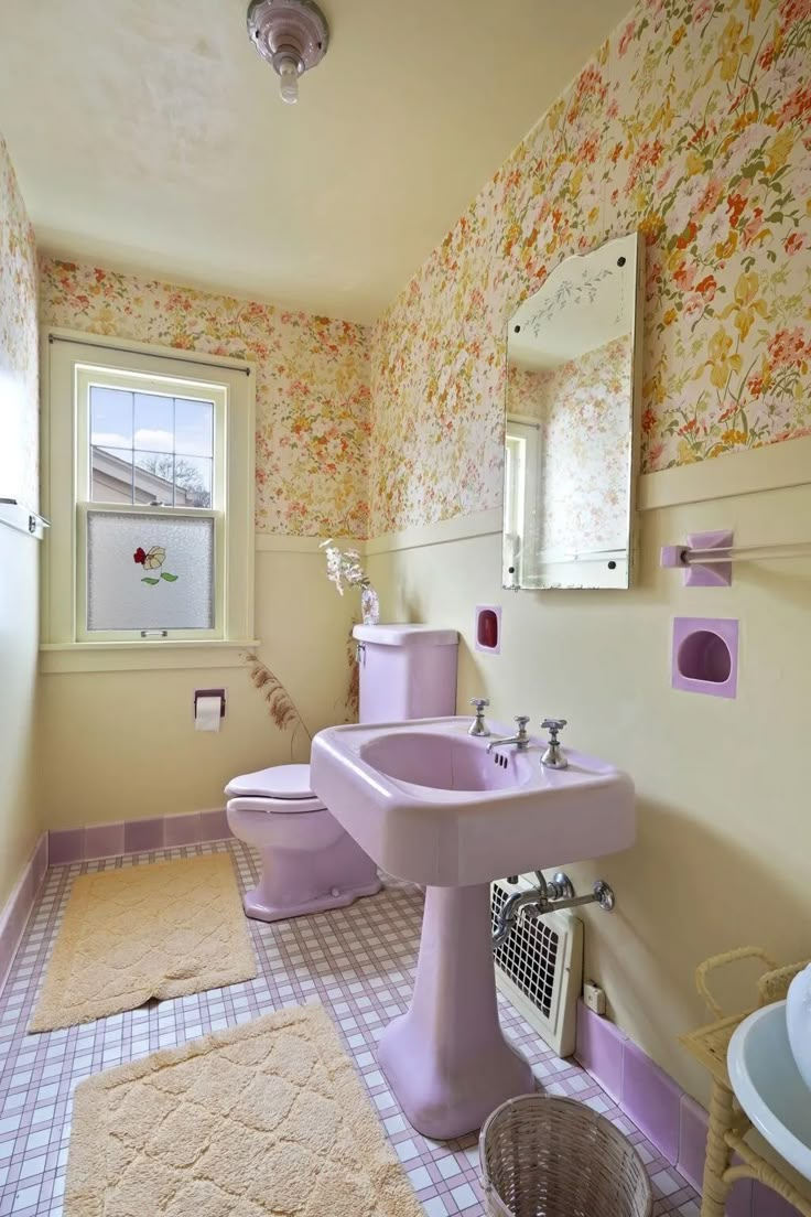 a bathroom with pink fixtures and floral wallpaper on the walls, along with a toilet and sink