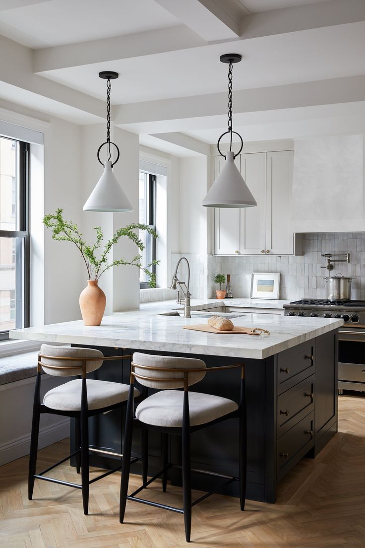 a kitchen with two pendant lights hanging from the ceiling and stools at the island