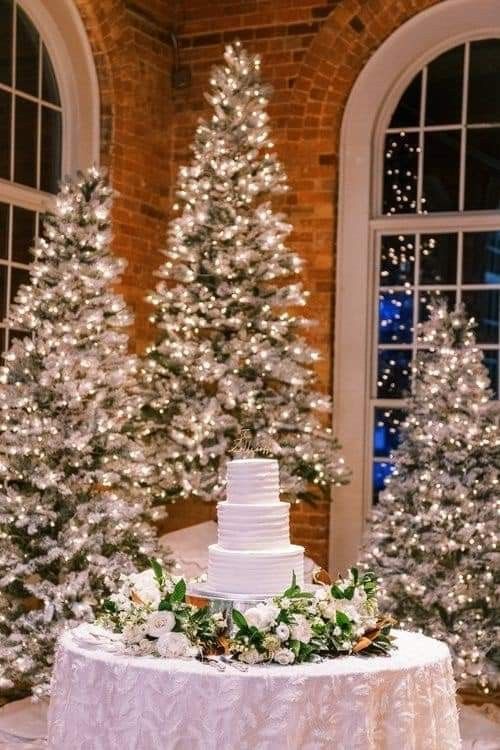 a white wedding cake sitting on top of a table in front of trees with lights