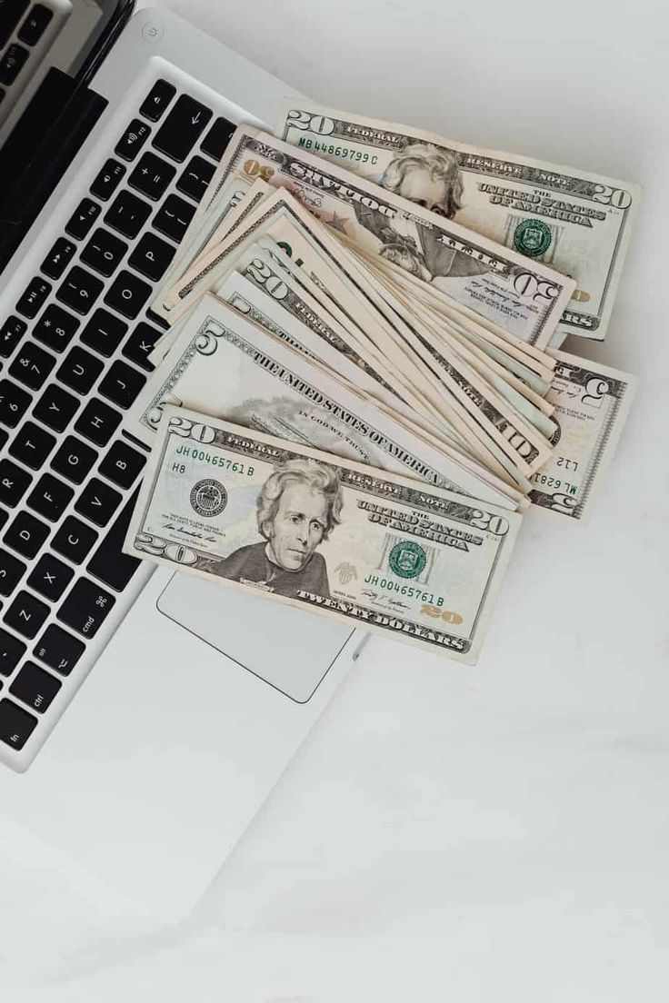 a laptop computer sitting on top of a white table next to stacks of dollar bills