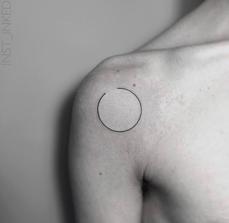 a black and white photo of a person's shoulder with a small circle tattoo on it