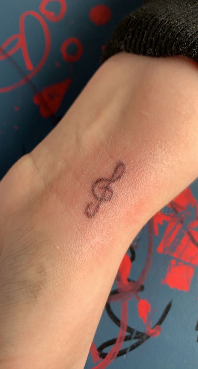 a small tattoo on the wrist of a person's left hand, with an arrow in the middle