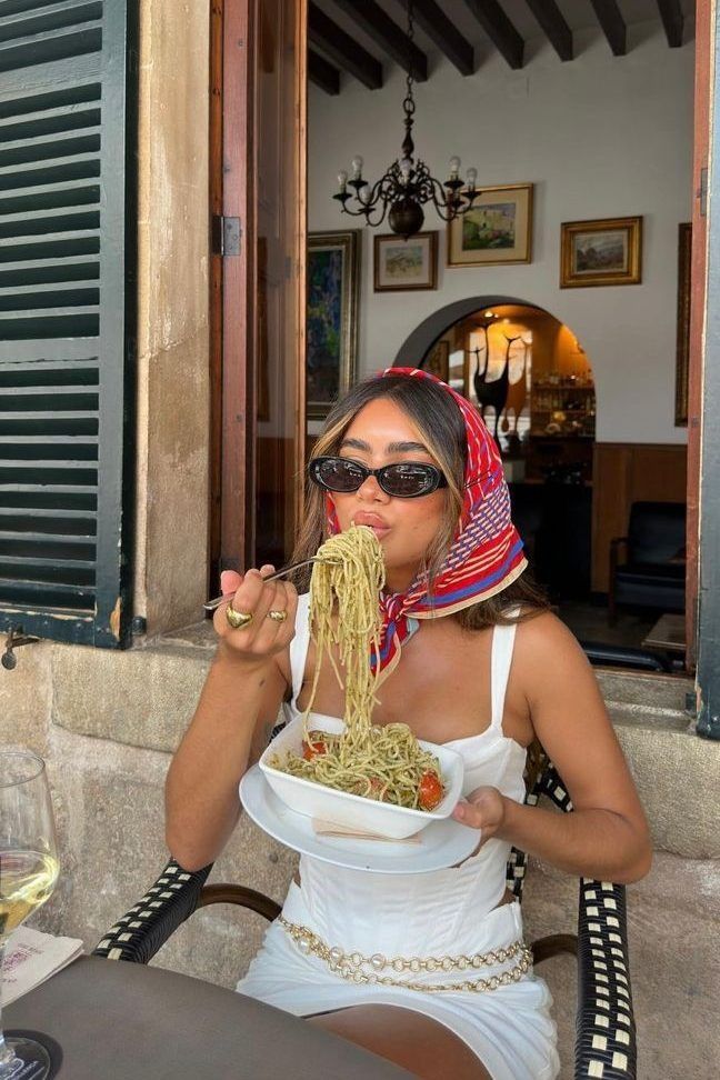 a woman sitting at a table eating some food from a bowl with her hands in her mouth