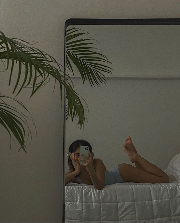 a woman laying in bed taking a selfie with her cell phone and palm tree