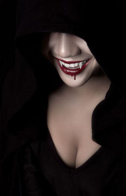 a woman with blood on her face wearing a black hoodie and vampire makeup is looking at the camera