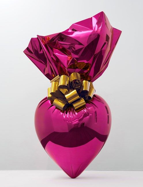 a shiny pink heart shaped vase with gold bow