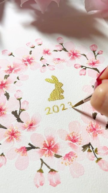 a person is painting flowers on paper with gold paint and a rabbit in the center