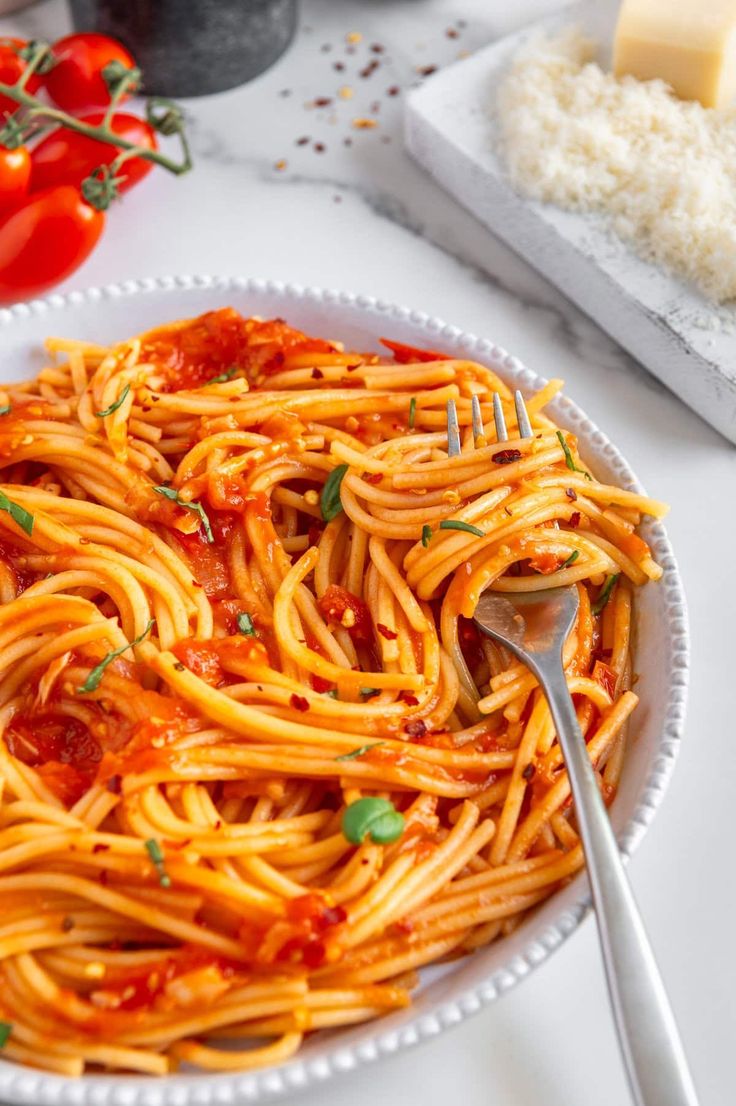 a plate full of spaghetti with sauce and parmesan cheese on the side next to tomatoes