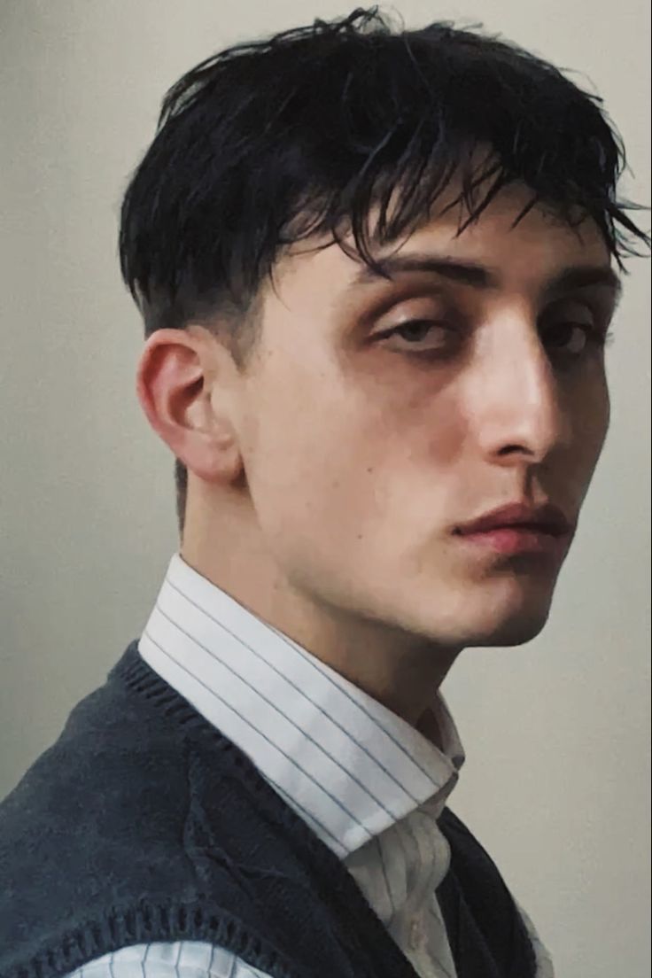 a young man with black hair wearing a vest and striped shirt looking at the camera