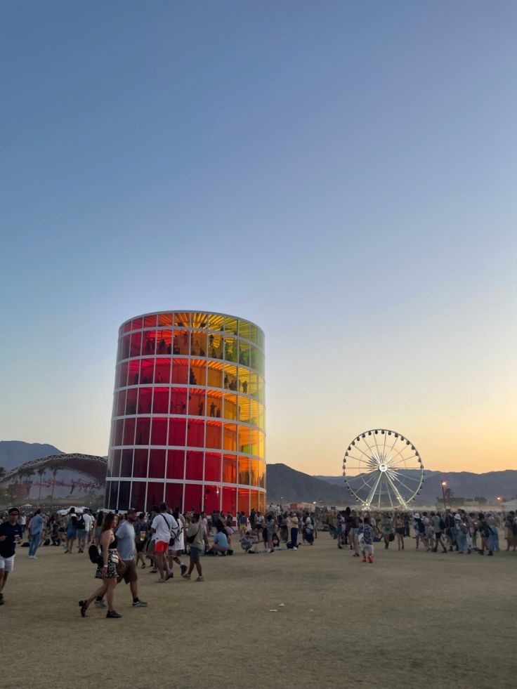 many people are walking around in front of a colorful building with a ferris wheel behind it