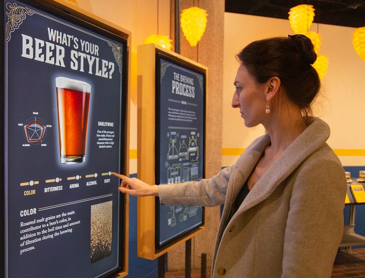 a woman pointing to a poster with a pint of beer in front of it