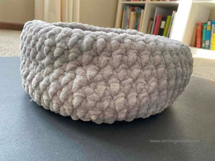 a knitted bowl sitting on top of a table next to a book shelf with books in the background