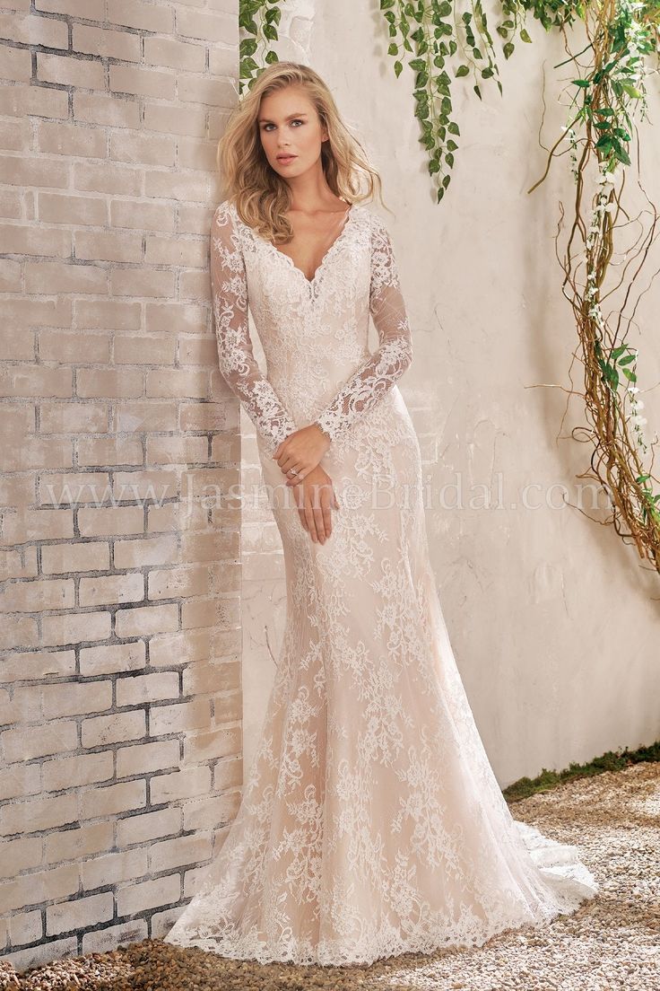 a woman standing in front of a brick wall wearing a long sleeved wedding dress