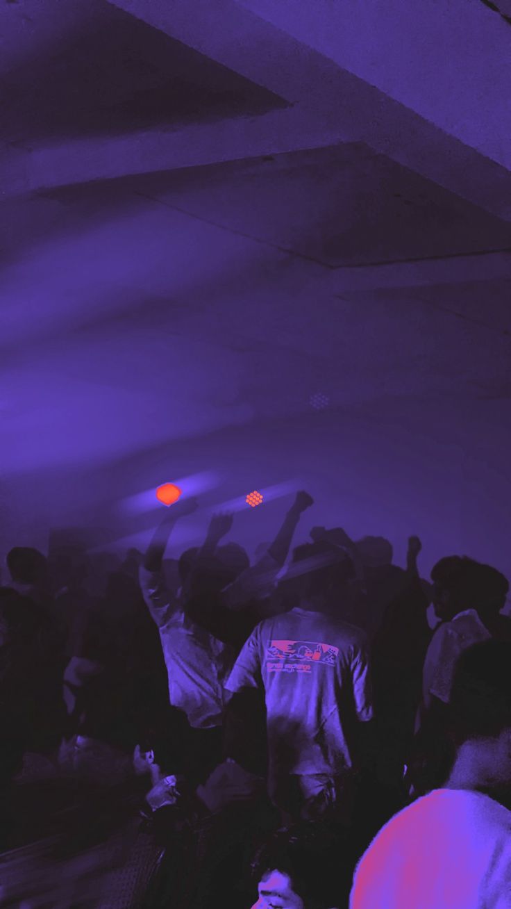 a group of people standing around each other in a room with purple lighting on the ceiling