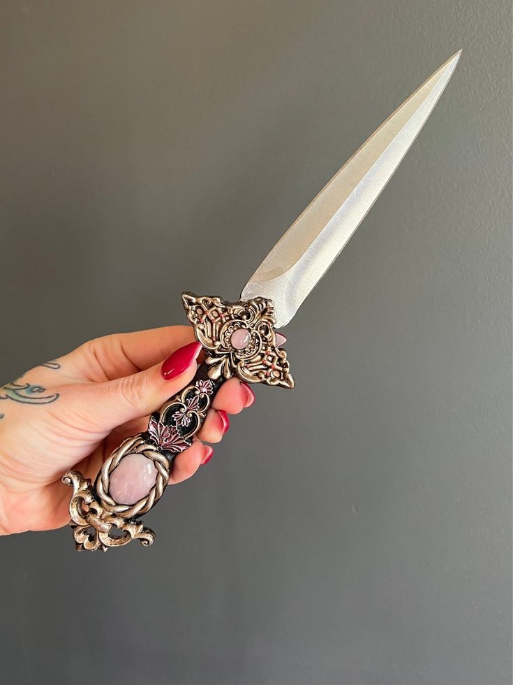 a person holding a knife with an ornate handle and decoration on the blade, in front of a gray wall