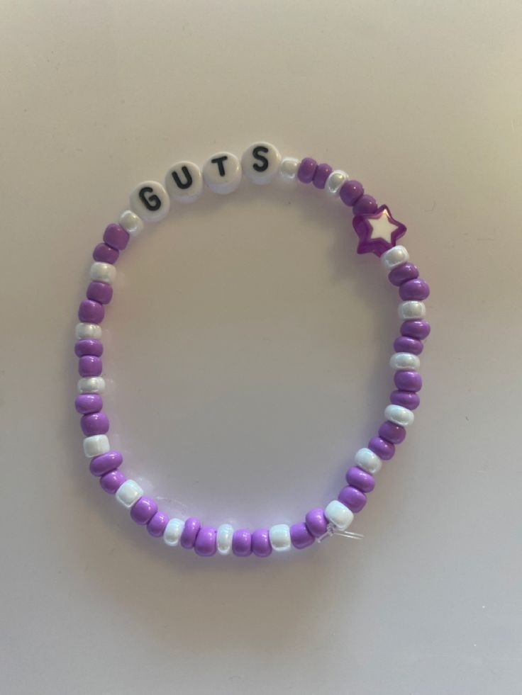 a purple and white beaded bracelet with the word guts written in small letters on it