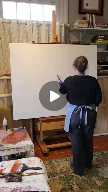 a woman standing in front of an easel holding a paintbrush and drawing on a white board