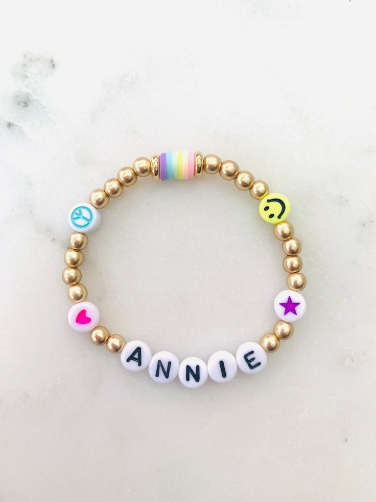 🌈 Colorful emoji beads with matte gold accents make this name bracelet one of the cutest. Can be made in adult or child sizes. Please note name/word and any color preference of the heart, star or peace sign in the personalization section. 🌈 Listing is for ONE bracelet.  🌈 Sizing length is as follows:  Women's small: 6.5 inches Women's medium: 7 inches Women's large: 7.5 inches Women's XL: 8 inches Children's 4-5 years old: 5.75 inches Children's 6-7 years old: 6 inches Children's 8-9 years old: 6.25 inches Children's 10-13 years old: 6-7 inches **Please measure wrist before ordering. Bracelets are stretchy but you do not want them to be super loose around your wrist.  🌈 All orders are FINAL SALE. These are custom bracelets made to order. PLEASE DOUBLE CHECK ALL SPELLING AND COLOR SELEC Trendy Personalized Charm Bracelet For Birthday, Personalized Trendy Charm Bracelet For Birthday, Cute Name Bracelet With Round Beads For Everyday, Cute Everyday Name Bracelet With Round Beads, Cute Personalized Gold Stretch Bracelet, Customizable Fun Jewelry For Everyday, Personalized Cute Gold Beaded Bracelets, Personalized Fun Beaded Bracelets For Everyday, Trendy Name Bracelet For Birthday