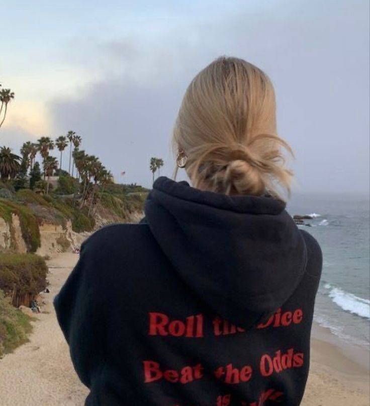 a woman is standing on the beach looking at the water and palm trees in the distance