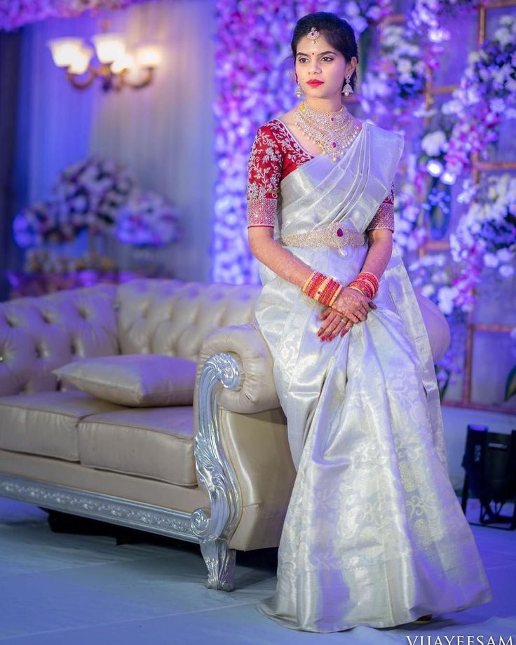 a woman in a white and red sari sitting on a couch with purple flowers behind her