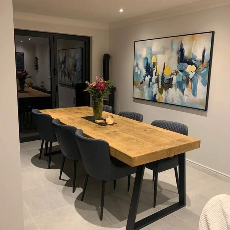 a dining room table with blue chairs and a painting on the wall