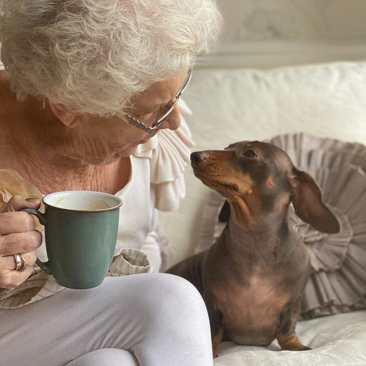 a woman sitting on a couch with her dog and holding a coffee cup in front of her