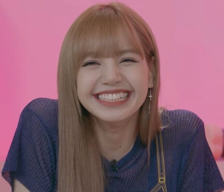 a woman with long hair smiling and wearing a blue shirt in front of a pink wall