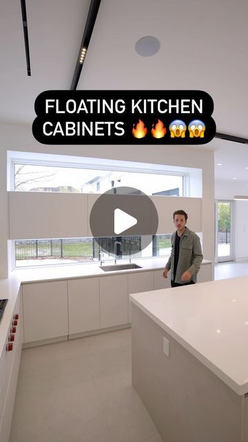 a man standing in the middle of a kitchen with white counter tops and cabinets on each side