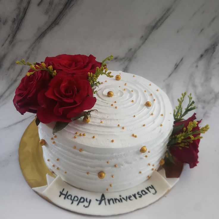 a white cake decorated with red roses and gold sprinkles on a marble table