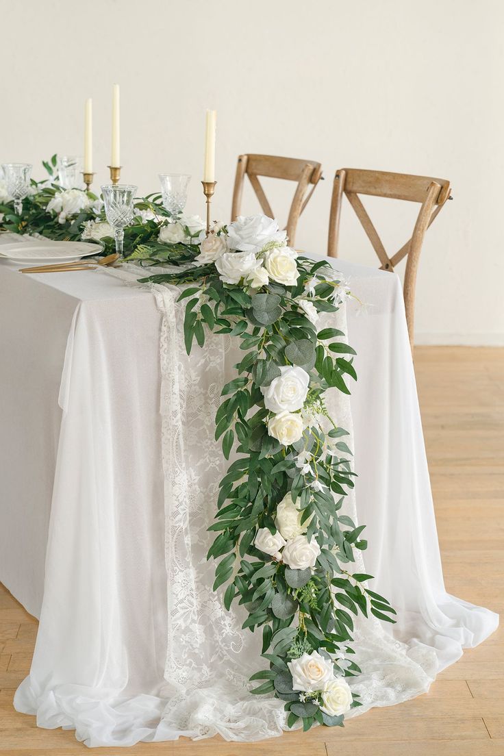 the table is set with white flowers and greenery, along with candles on it