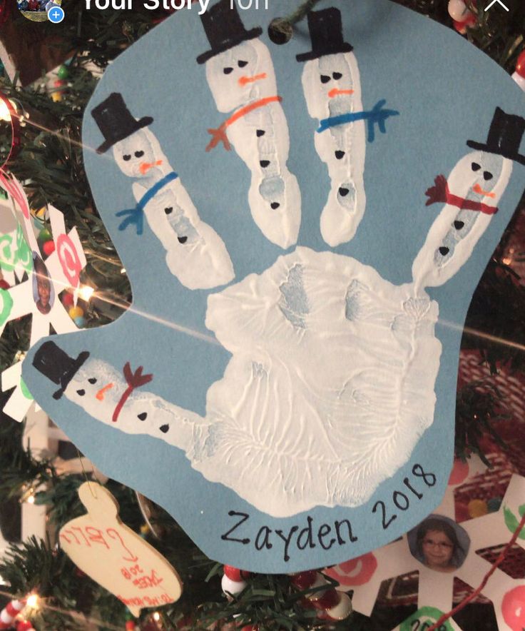 a handprint ornament hanging from a christmas tree with snowmen on it