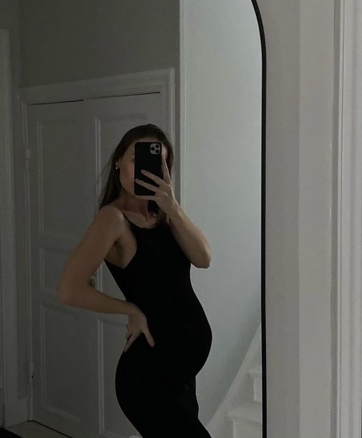 a pregnant woman taking a selfie in front of a mirror with her cell phone