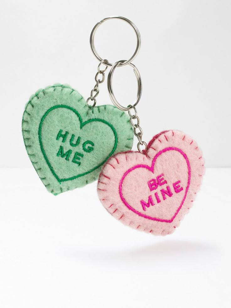 two heart shaped key chains with the words hug me and be mine written on them