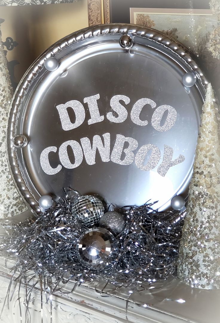 a disco cowboy sign sitting on top of a mantle next to silver balls and tinsel