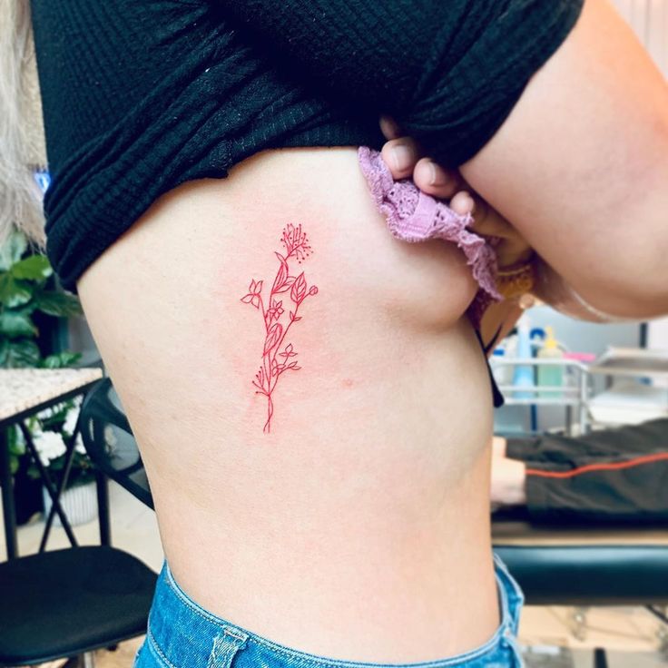 a woman's stomach with a small pink flower tattoo on her lower side ribcage