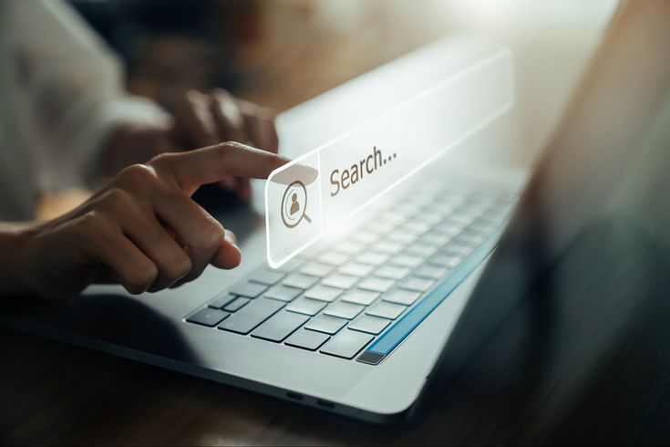 someone using a laptop computer with the word search on its screen and their hand pointing at it