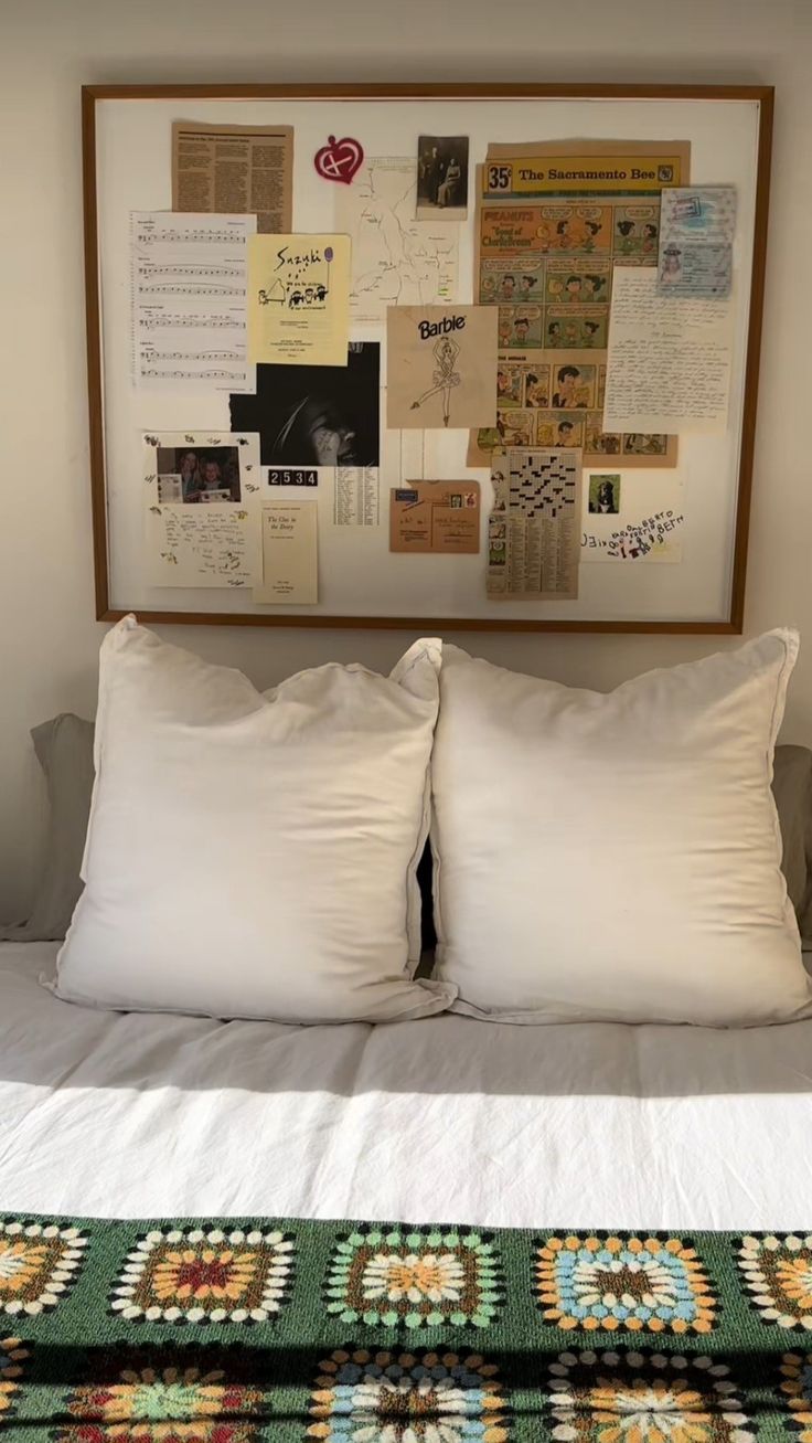 a bed with two white pillows on top of it next to a framed piece of paper