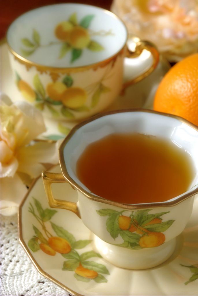 a cup of tea next to an orange on a saucer and plate with flowers