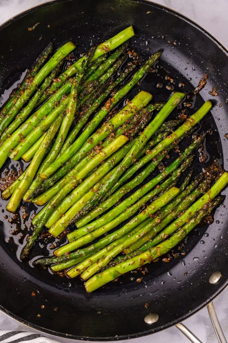 asparagus being cooked in a skillet with seasoning on the side, ready to be eaten