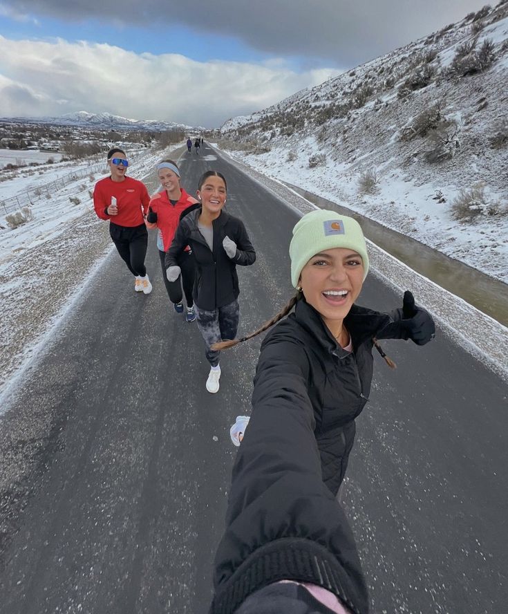 three people are running in the snow on a road and one is taking a selfie