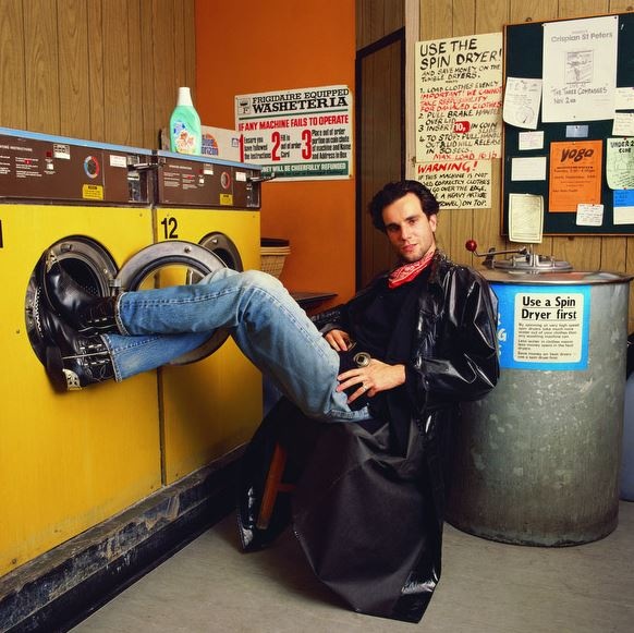 a man sitting in front of a dryer next to a yellow washer machine