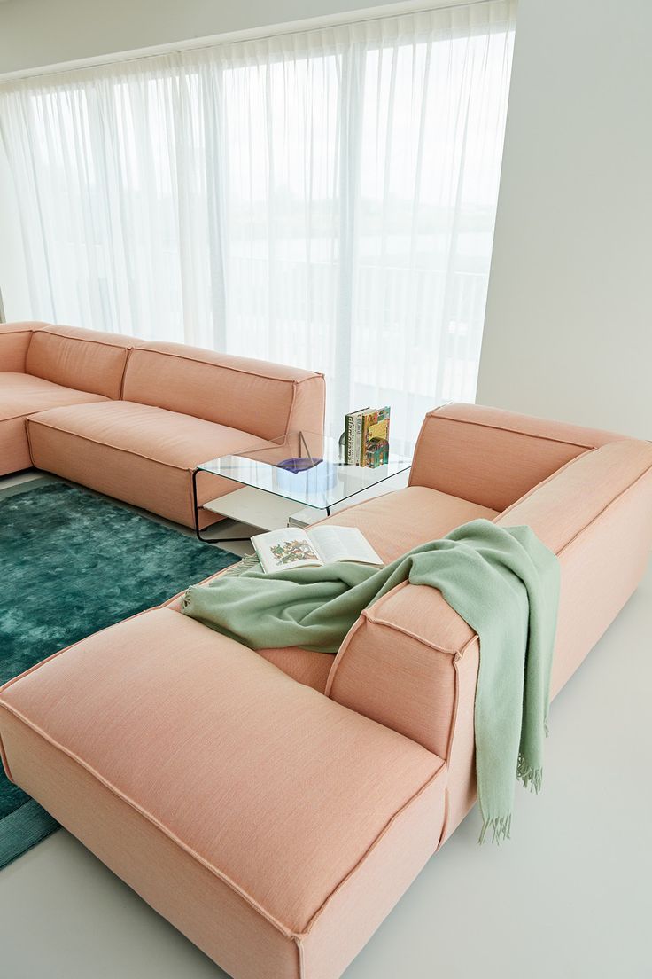 a living room with a large sectional couch and green rugs on the floor in front of a window