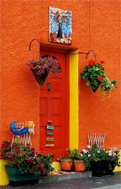 an orange building with potted plants on the outside and a red door in front