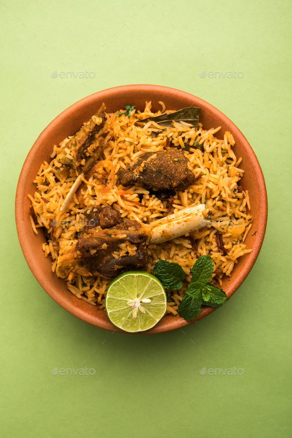 a bowl filled with rice and meat on top of a green table next to a slice of lime