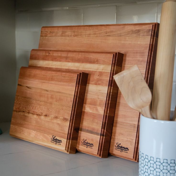 three chopping boards sitting on top of a counter next to a mug and knife