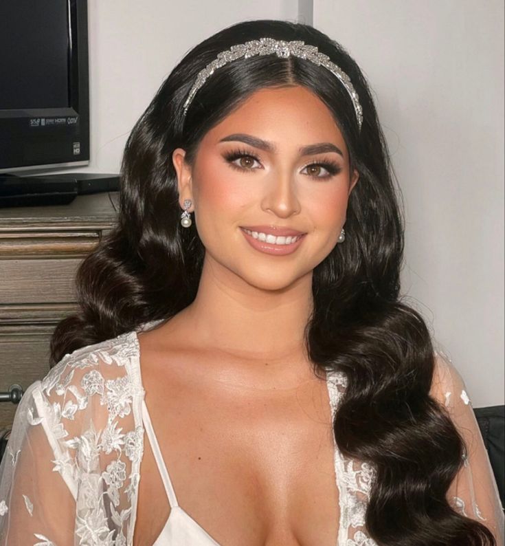 a woman with long dark hair wearing a tiara and posing for the camera in front of a tv