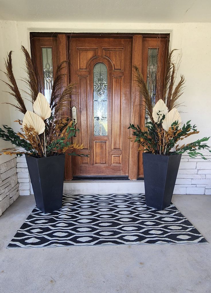 two large planters with flowers are on the front door mat in front of a wooden door