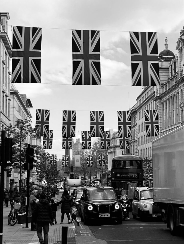 black and white photograph of people walking on the street with union jack flags hanging above them