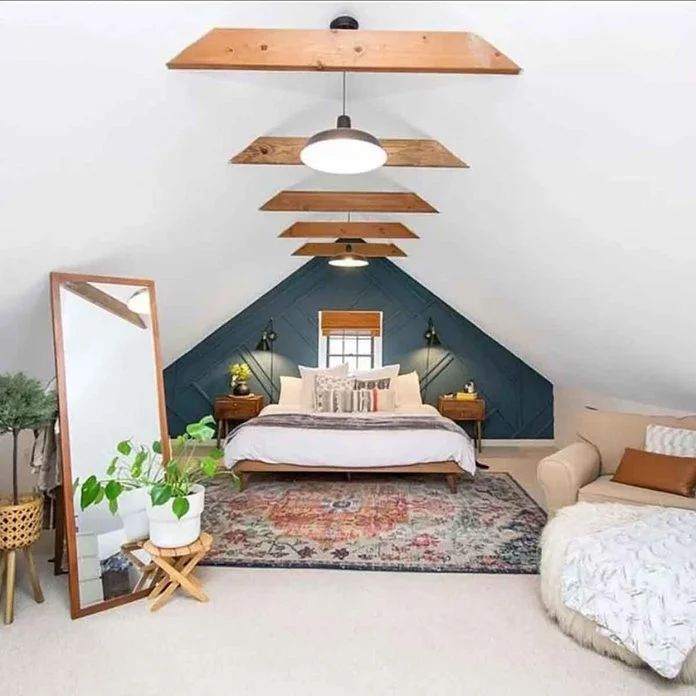 an attic bedroom with a bed, mirror and two chairs in it's corner